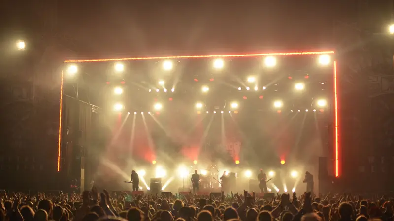 A band on a lit stage, seen over a full crowd.